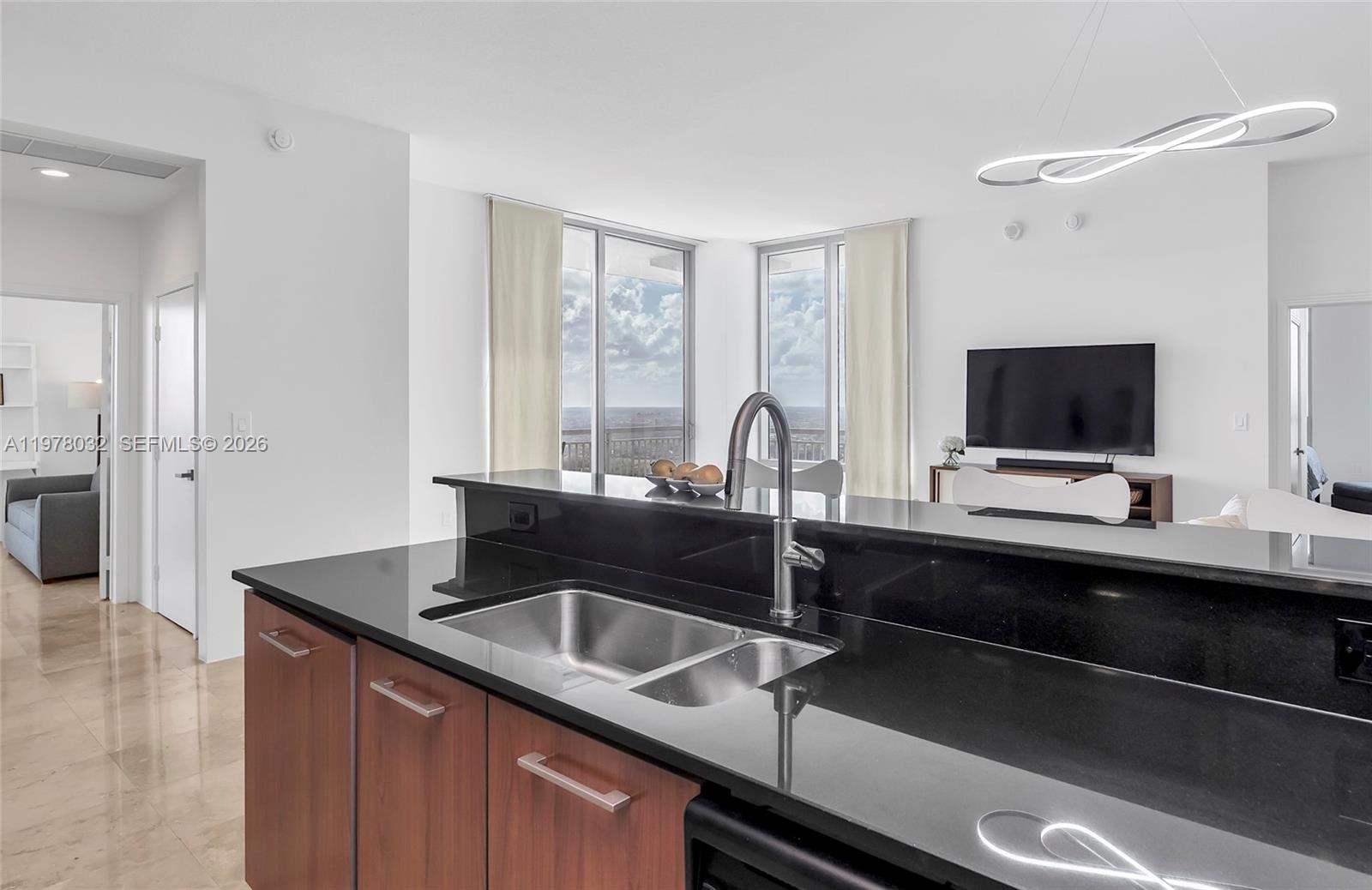 A modern kitchen with black countertops and wood cabinets overlooks a bright living area — 9066 SW 73rd Ct, Miami FL 33156, MIAMI, FL