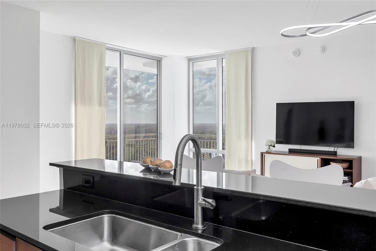 A kitchen island with a black countertop and sink overlooks a living area with windows — 9066 SW 73rd Ct, Miami FL 33156, MIAMI, FL