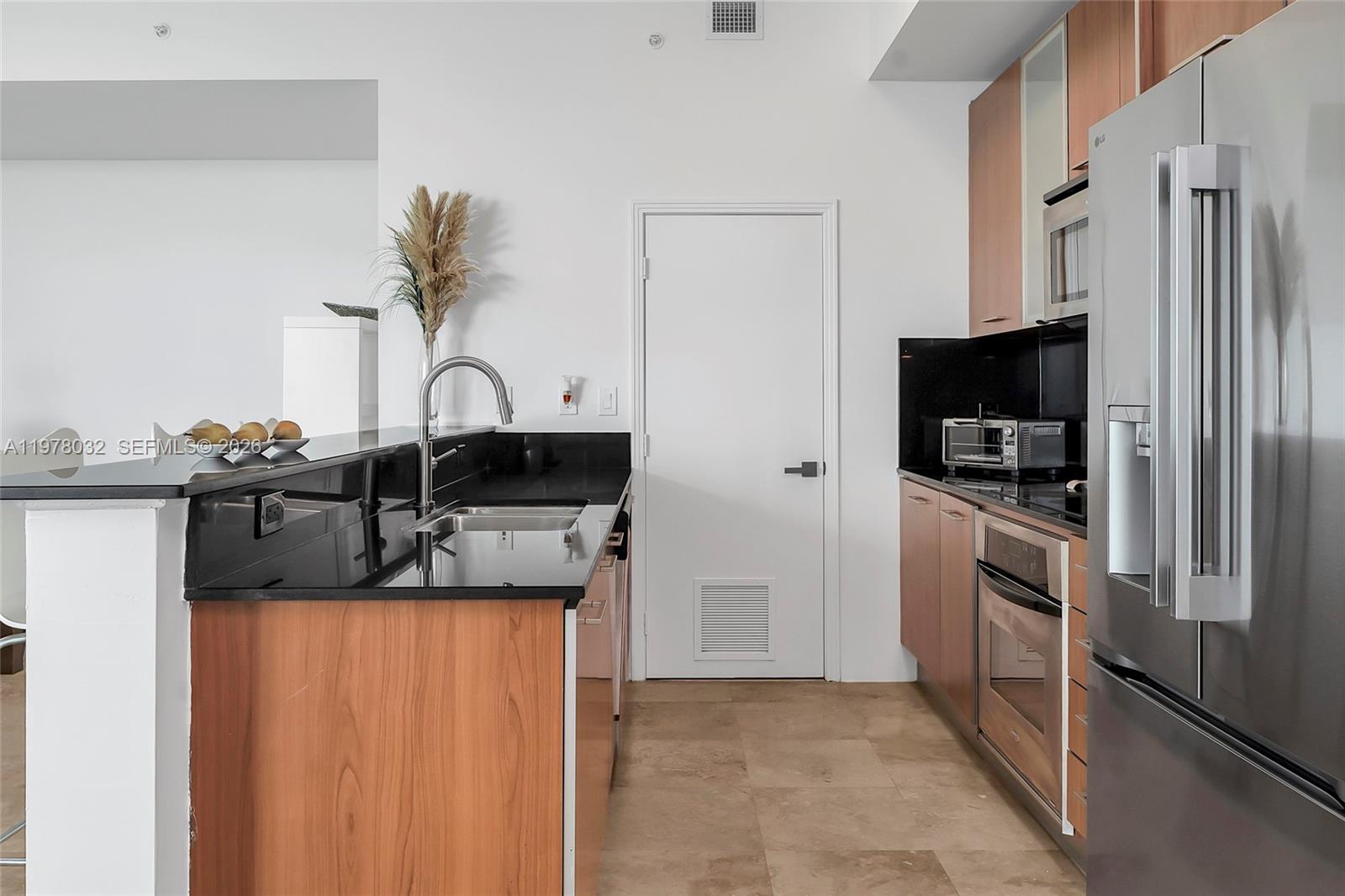 A kitchen features wood cabinets, black countertops, stainless steel appliances, and a central sink — 9066 SW 73rd Ct, Miami FL 33156, MIAMI, FL