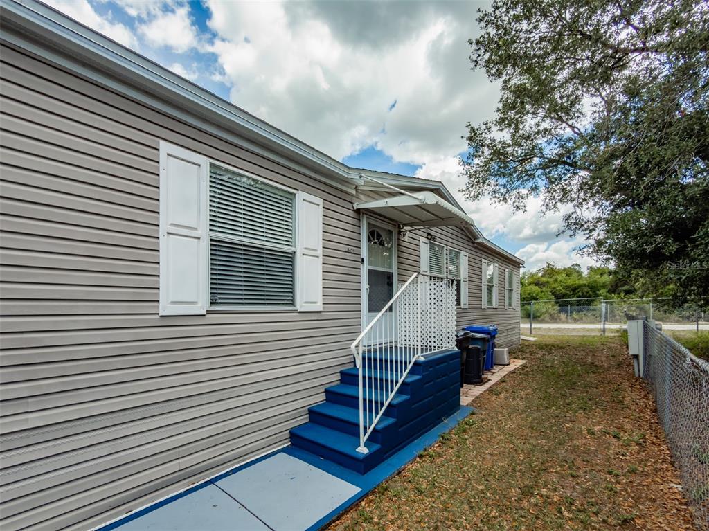 The exterior of a manufactured home features light gray siding, blue steps, and white shutters — 8471 FANTASIA PARK WAY, RIVERVIEW, FL