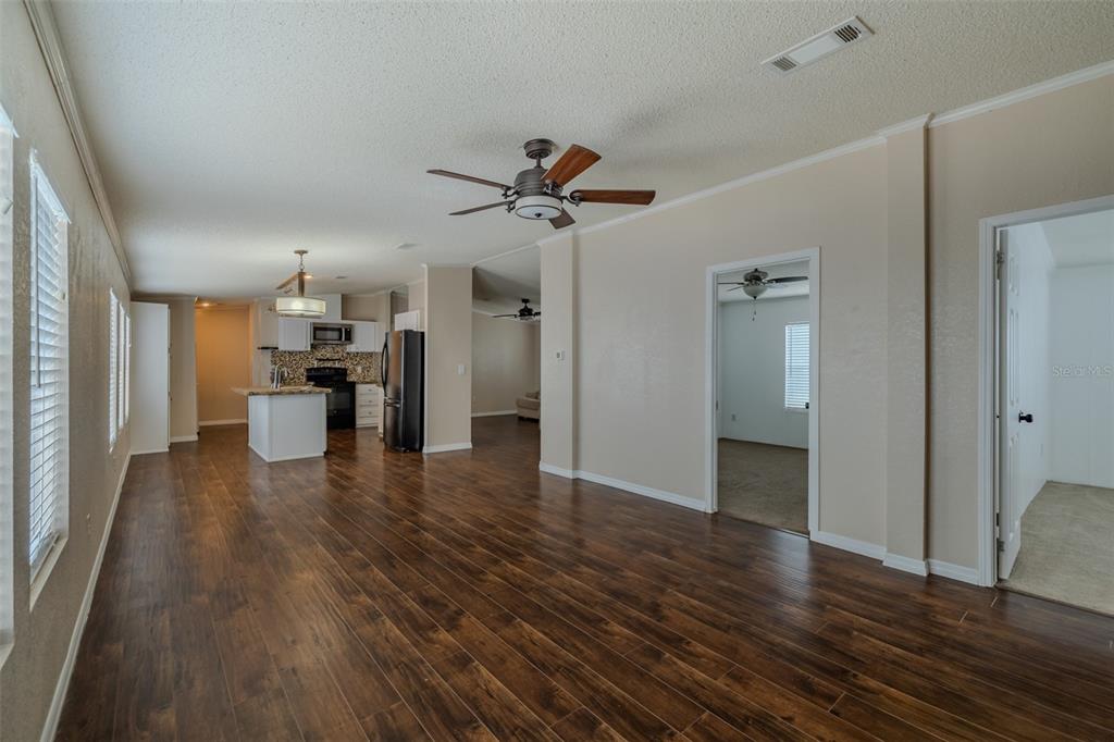 A spacious living area with dark wood-look flooring, a ceiling fan, and an open kitchen — 8471 FANTASIA PARK WAY, RIVERVIEW, FL