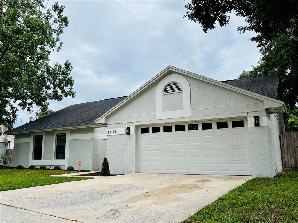 A single-story house with a white stucco exterior, a two-car garage, and a dark roof — 1045 SHAFFER TRAIL, OVIEDO, FL