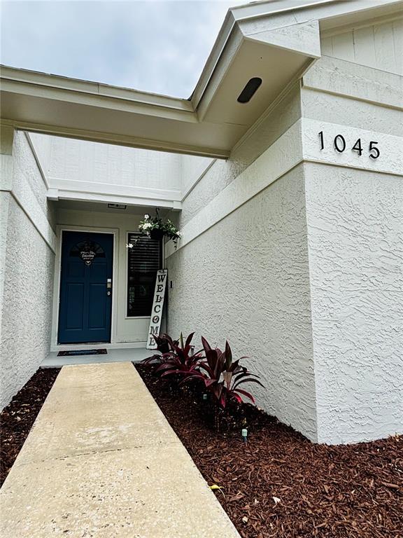 A concrete walkway leads to a blue front door with a welcome sign and plants — 1045 SHAFFER TRAIL, OVIEDO, FL