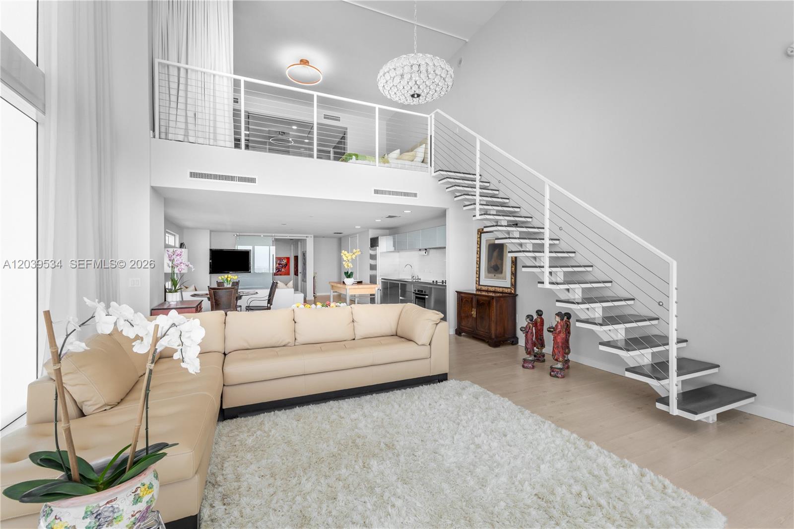 A modern living room features a beige sectional sofa, a white rug, and a floating staircase — 1040 Biscayne Blvd # 3101, Miami FL 33132, MIAMI, FL