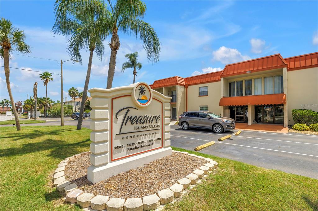 A sign for Treasure Island Villas Condominiums stands in front of a multi-story apartment building — 10375 PARADISE BOULEVARD UNIT 51, TREASURE ISLAND, FL
