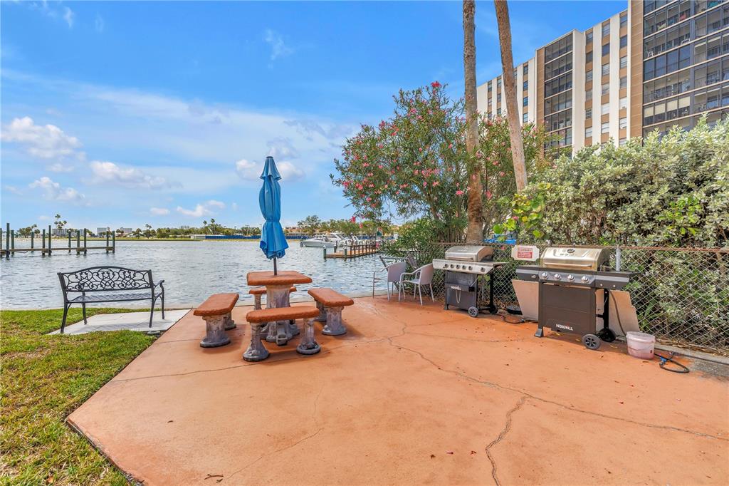 A waterfront patio features a picnic table with an umbrella, a bench, and two outdoor grills — 10375 PARADISE BOULEVARD UNIT 51, TREASURE ISLAND, FL