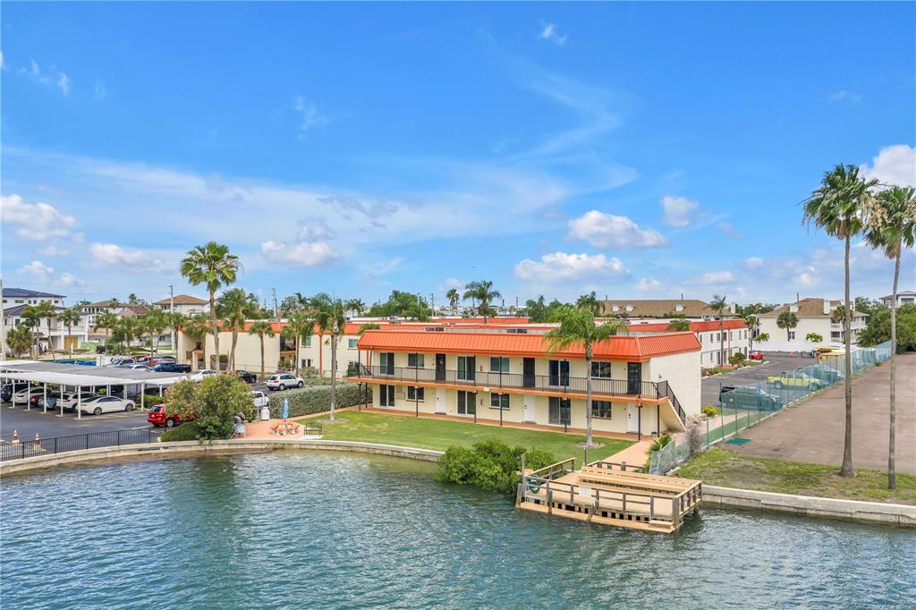 An exterior view of a two-story apartment building with a red roof beside a canal — 10375 PARADISE BOULEVARD UNIT 51, TREASURE ISLAND, FL