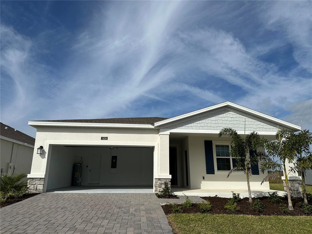A single-story house exterior features a two-car garage, stone accents, and a paved driveway — 1656 CONTENTMENT LOOP, KISSIMMEE, FL