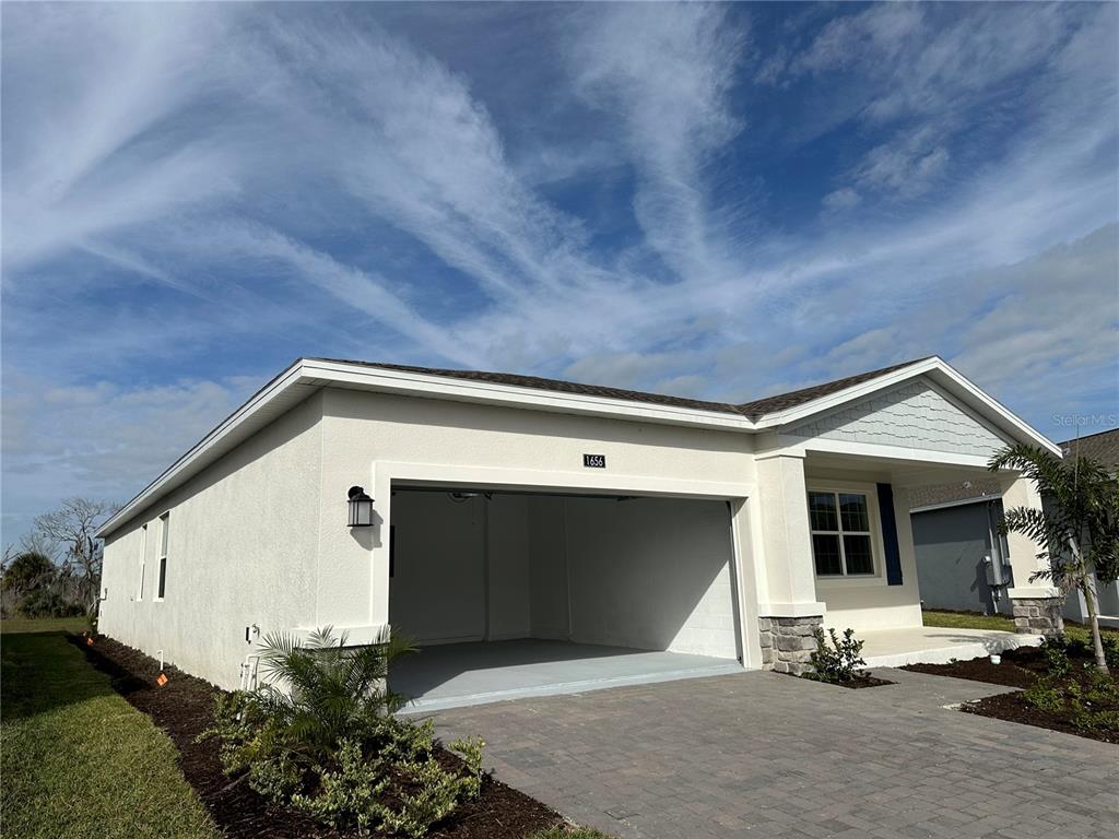 A single-story house exterior features a two-car garage, light stucco walls, and a paved driveway — 1656 CONTENTMENT LOOP, KISSIMMEE, FL