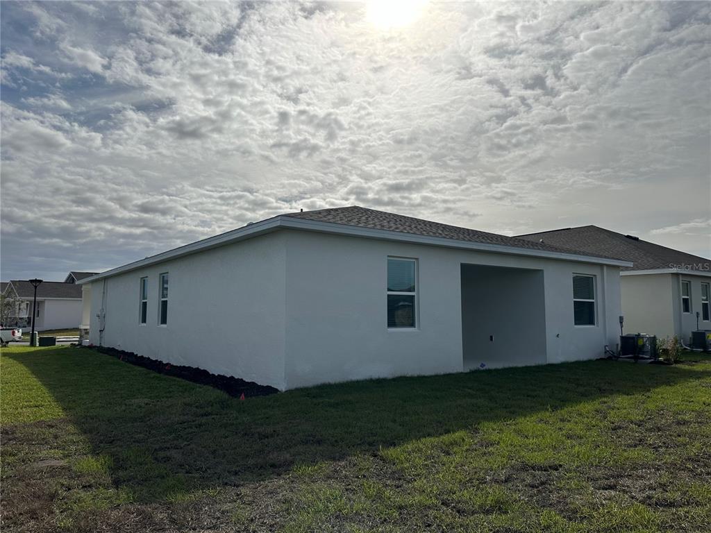 The rear exterior of a white stucco house features a covered patio and lawn — 1656 CONTENTMENT LOOP, KISSIMMEE, FL