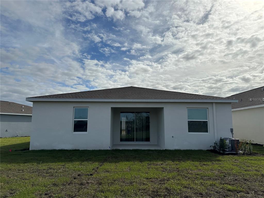 The rear exterior of a single-story house features a covered patio and sliding glass doors — 1656 CONTENTMENT LOOP, KISSIMMEE, FL