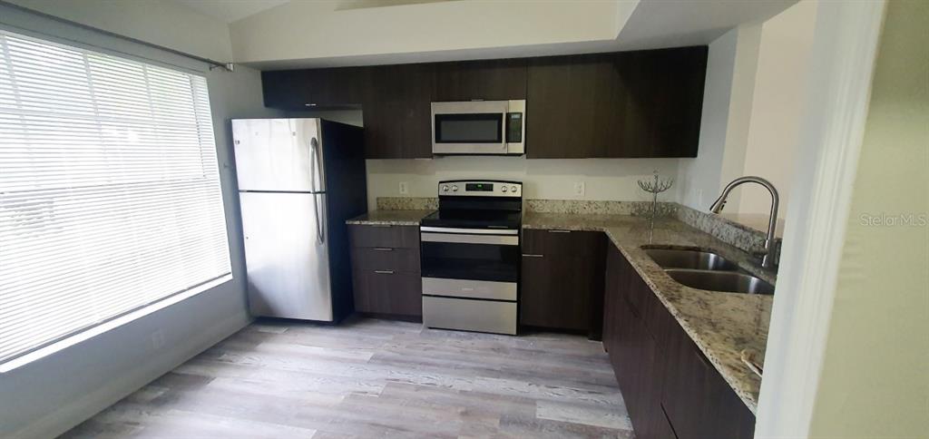 A kitchen features dark wood cabinets, stainless steel appliances, and granite countertops — 1215 BAREFOOT BAY DRIVE, ORLANDO, FL