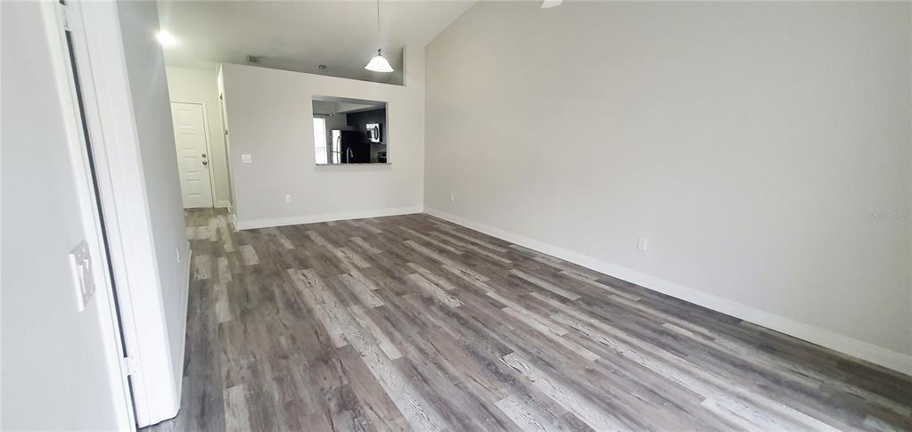 An empty living room features light gray walls, wood-look flooring, and a kitchen pass-through window — 1215 BAREFOOT BAY DRIVE, ORLANDO, FL