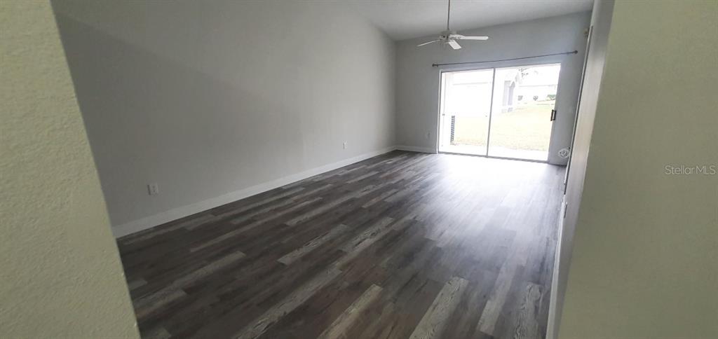 An empty room features wood-look flooring, a ceiling fan, and sliding glass doors to outside — 1215 BAREFOOT BAY DRIVE, ORLANDO, FL