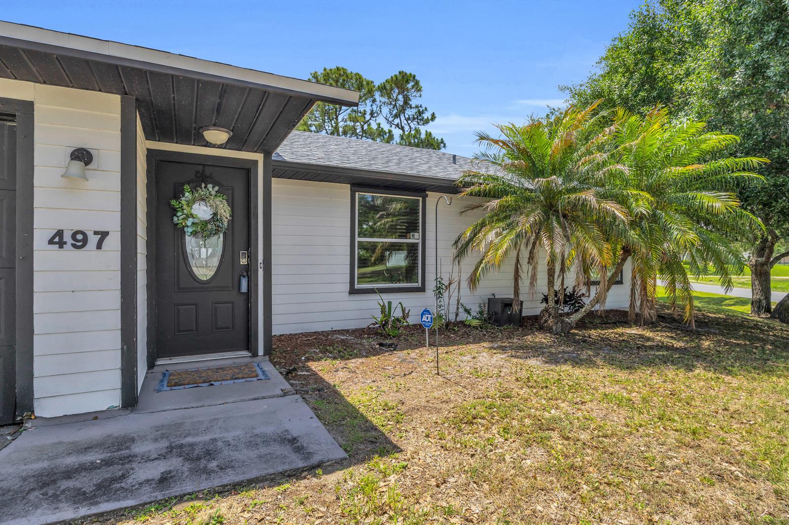 The exterior of a single-story house features white siding, a dark front door, and a palm tree — 497 Melrose Lane, Sebastian FL 32958, SEBASTIAN, FL