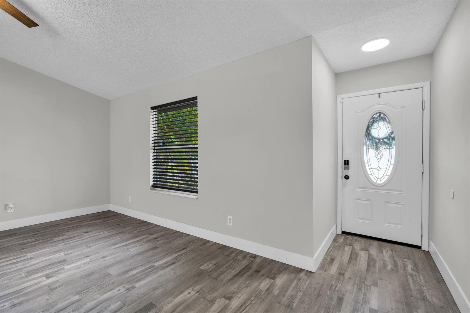 A room with gray walls, wood-look flooring, a window with blinds, and a white front door — 497 Melrose Lane, Sebastian FL 32958, SEBASTIAN, FL