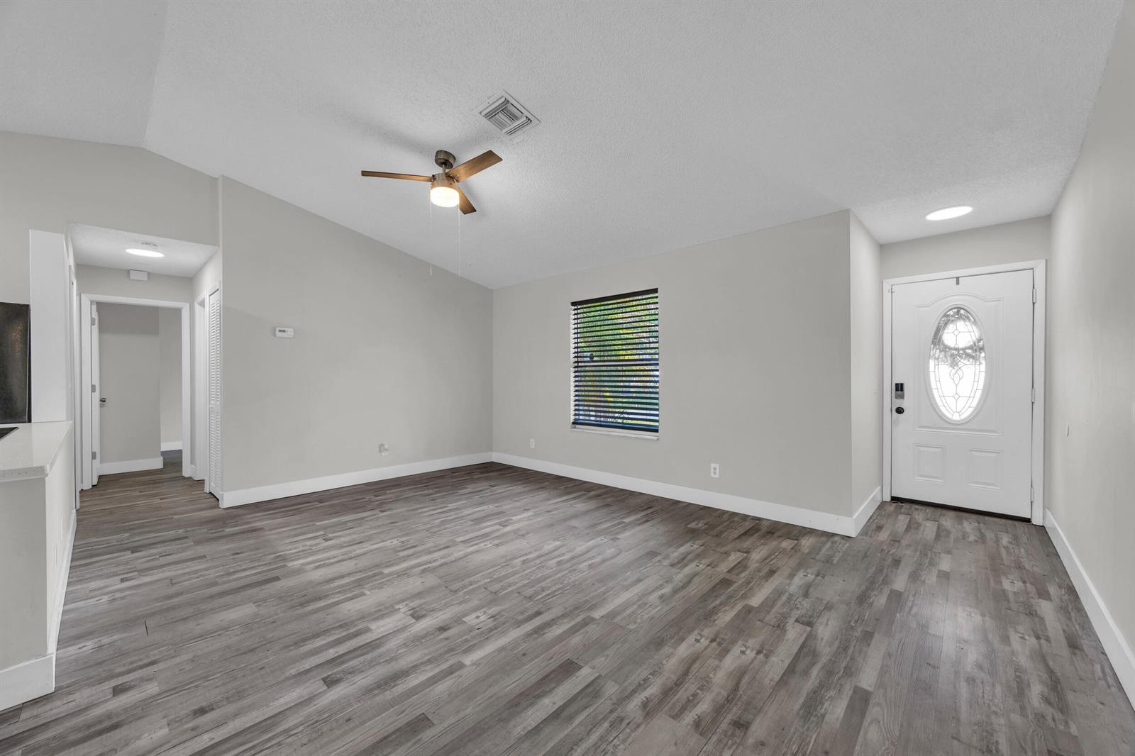 An empty living room features gray wood-look flooring, a ceiling fan, and a front door — 497 Melrose Lane, Sebastian FL 32958, SEBASTIAN, FL