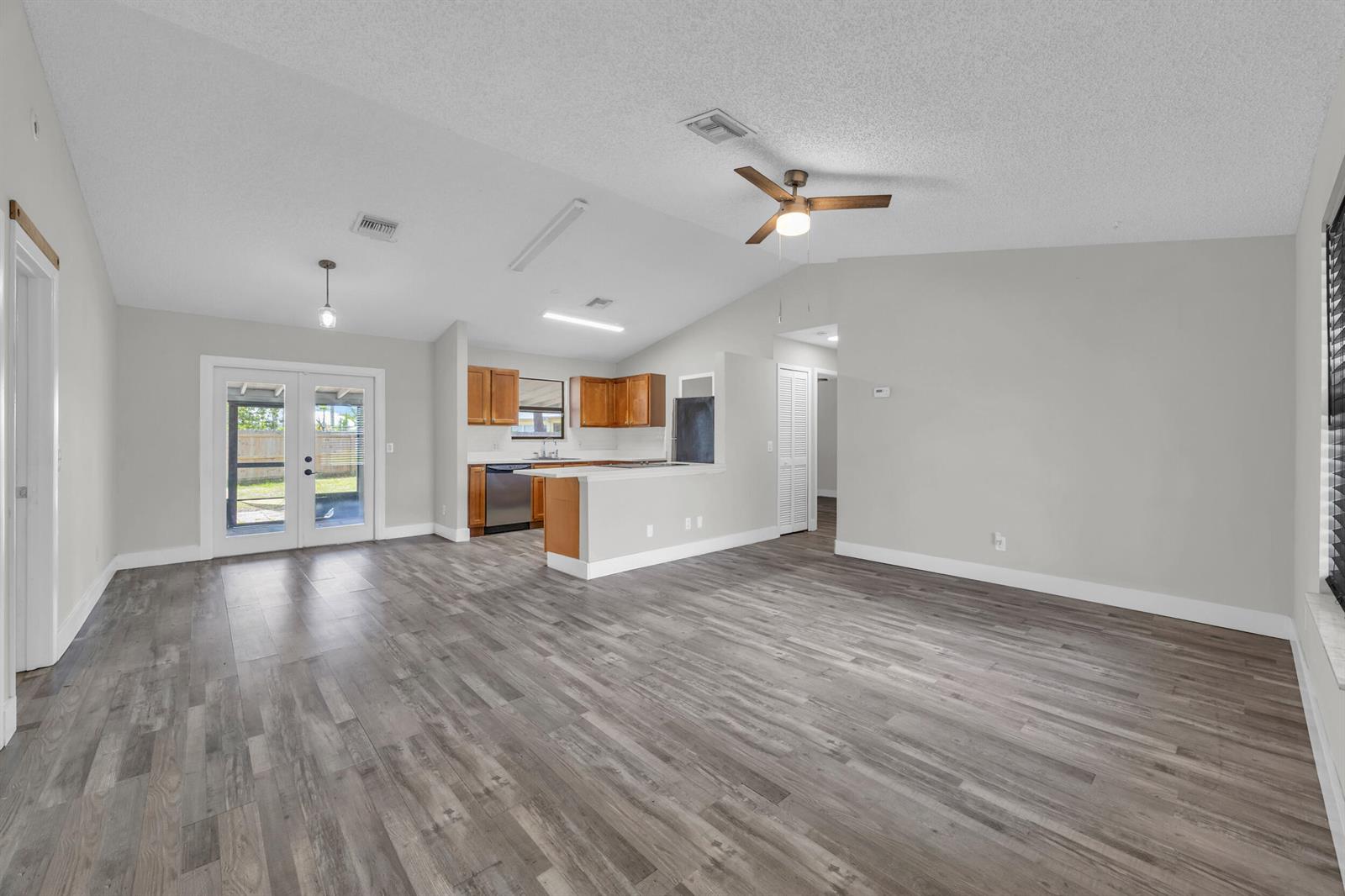 An open-concept living area features vaulted ceilings, wood-look flooring, and an adjacent kitchen — 497 Melrose Lane, Sebastian FL 32958, SEBASTIAN, FL