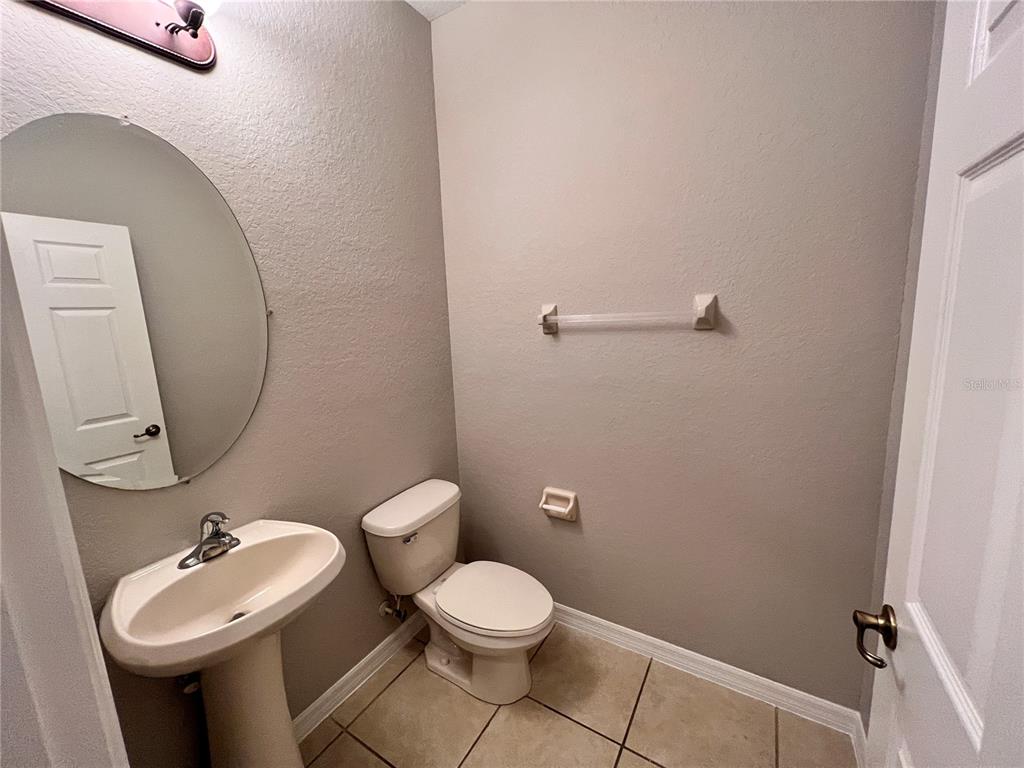 A small half bathroom features a pedestal sink, round mirror, and a white toilet — 2342 ALOHA BAY COURT, OCOEE, FL