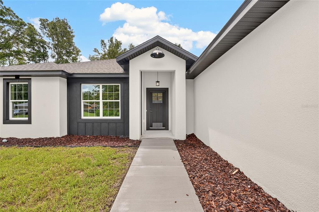 A modern house exterior features white stucco walls, dark trim, and a concrete walkway — 1 WALNUT DRIVE, OCALA, FL