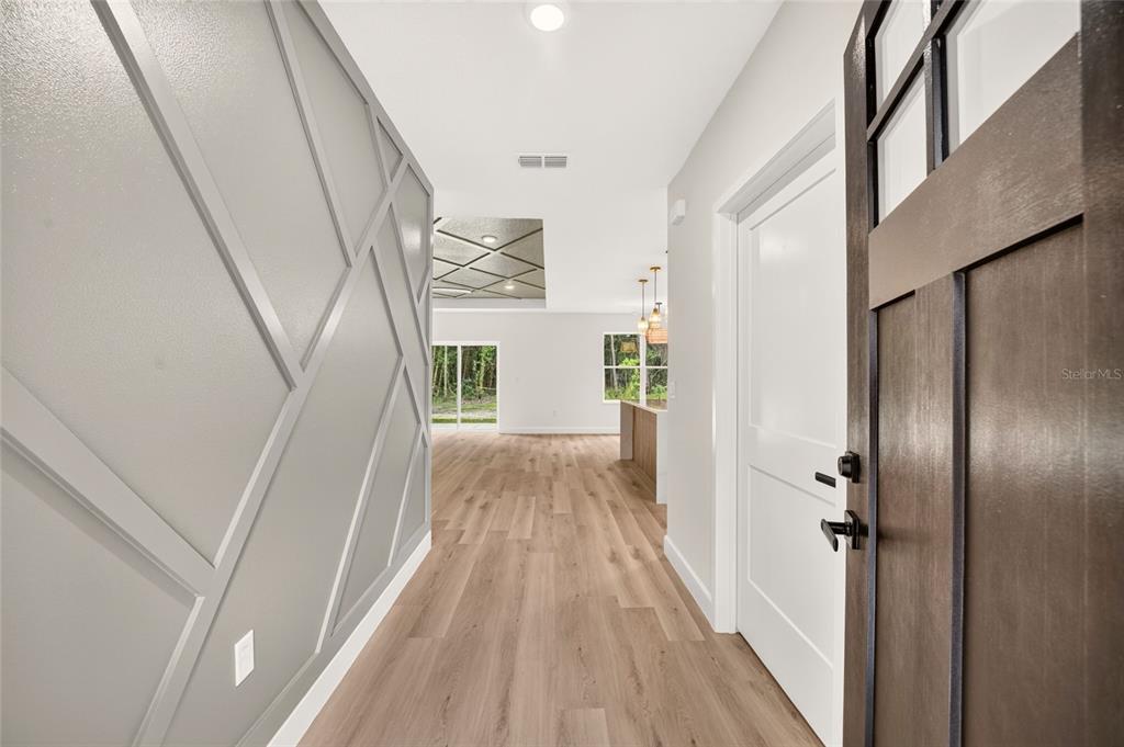An entryway features light wood flooring, a gray accent wall with geometric trim, and a door — 1 WALNUT DRIVE, OCALA, FL