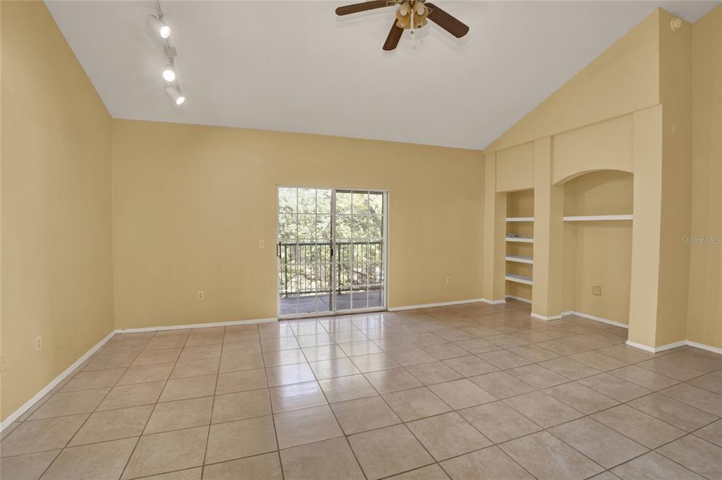 A living room with beige tile floors, vaulted ceilings, built-in shelving, and a sliding glass door — 1325 ROTONDA POINT UNIT 337, LAKE MARY, FL
