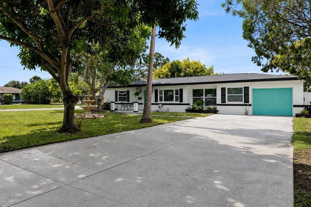 A white single-story house features a teal garage door, black shutters, and a front yard fountain — 4300 28TH AVENUE N, ST PETERSBURG, FL