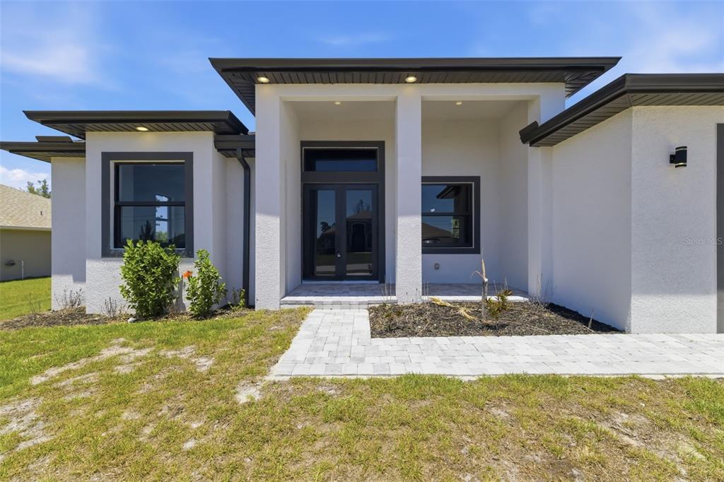 The exterior of a modern white house features a covered entryway with double glass doors — 15725 AUTRY CIRCLE, PORT CHARLOTTE, FL