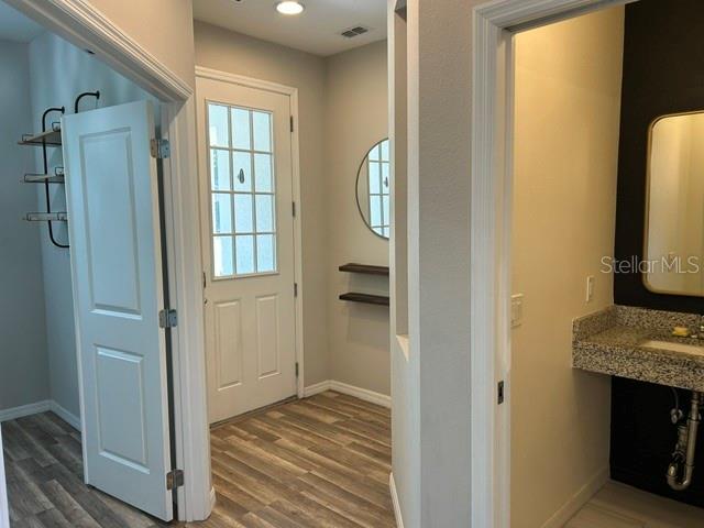 A hallway with wood-look flooring leads to an exterior door and a small bathroom — 3875 S FERN CREEK AVENUE, ORLANDO, FL
