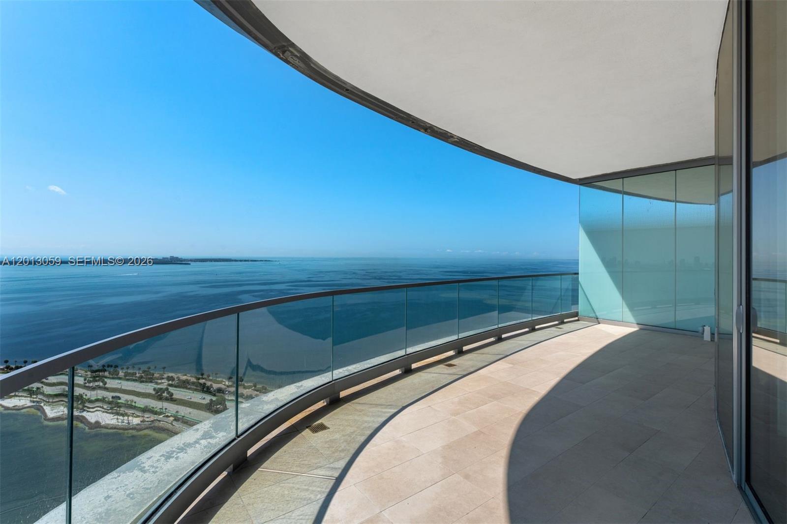 A curved balcony with lounge chairs overlooks a large body of water and city skyline — 175 SE 25 RD # 3601, Miami FL 33129, MIAMI, FL