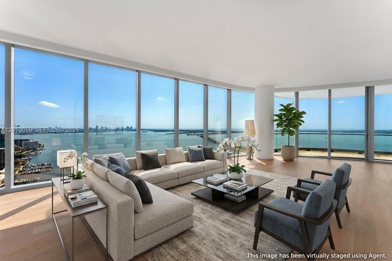 A modern living room features curved white furniture, a wooden coffee table, and floor-to-ceiling windows — 175 SE 25 RD # 3601, Miami FL 33129, MIAMI, FL