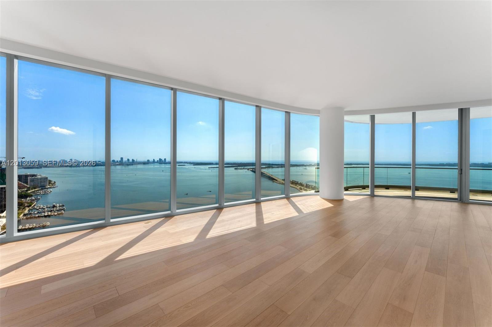 A modern living room features floor-to-ceiling windows, light wood flooring, and a curved sofa — 175 SE 25 RD # 3601, Miami FL 33129, MIAMI, FL