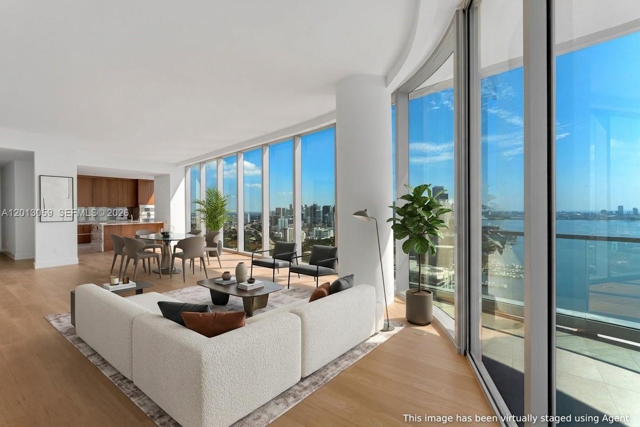 A modern living and dining area features floor-to-ceiling windows overlooking a bay and bridge — 175 SE 25 RD # 3601, Miami FL 33129, MIAMI, FL