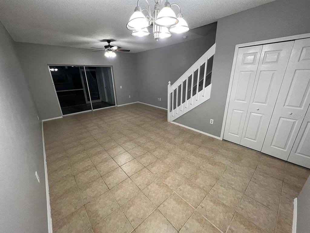 An empty room with tile flooring, a ceiling fan, a staircase, and sliding glass doors — 8674 HUNTERS KEY CIRCLE, TAMPA, FL