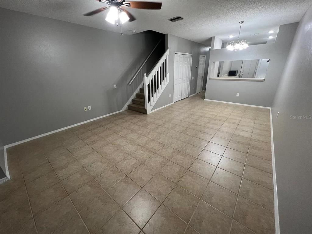 An open living area features gray walls, beige tile flooring, a staircase, and a ceiling fan — 8674 HUNTERS KEY CIRCLE, TAMPA, FL