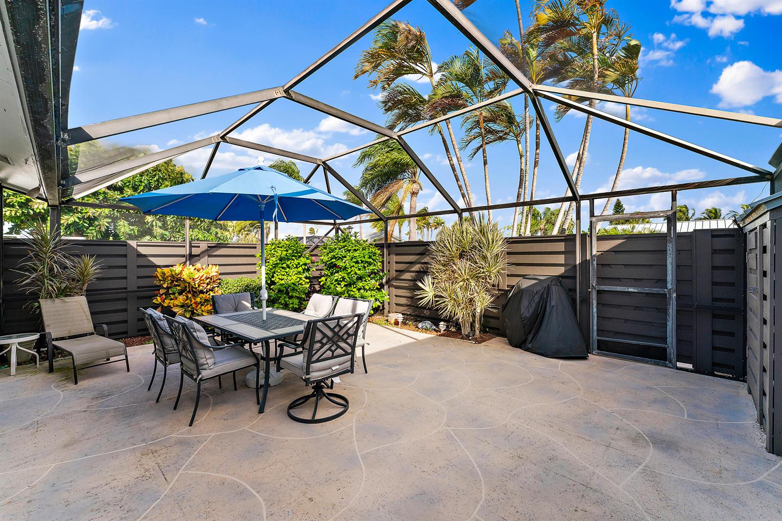 A screened-in patio features a dining set with a blue umbrella and palm trees — 1801 S Us Highway 1 # 9d, Jupiter FL 33477, JUPITER, FL