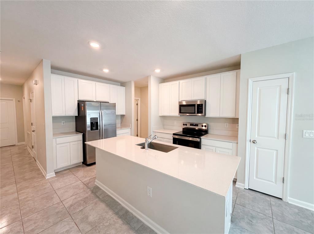 A kitchen features white cabinets, stainless steel appliances, a center island, and light-colored tile flooring — 2307 BURNEY FALLS LANE, DAVENPORT, FL