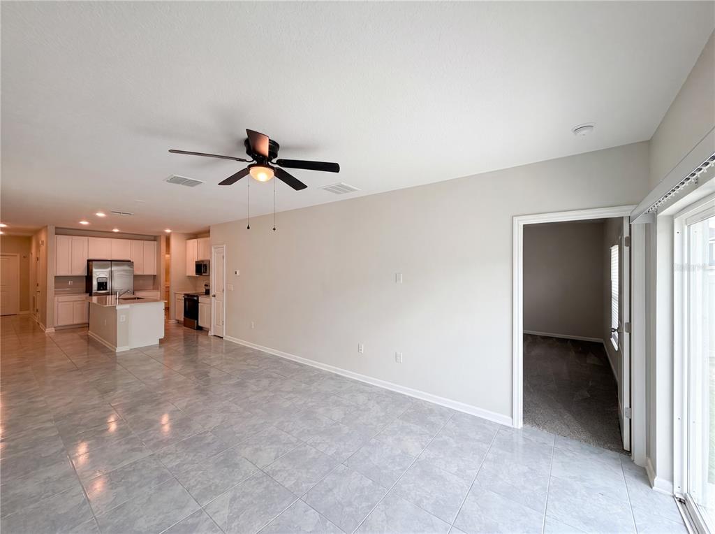 An open-concept living area features light-colored tile flooring, a ceiling fan, and an adjacent kitchen — 2307 BURNEY FALLS LANE, DAVENPORT, FL