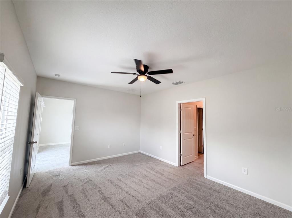An empty bedroom features gray carpet, light-colored walls, a ceiling fan, and two doorways — 2307 BURNEY FALLS LANE, DAVENPORT, FL
