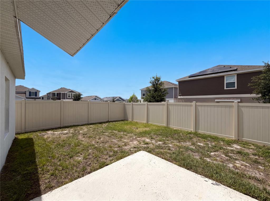 A fenced backyard features a concrete patio and patches of grass under a clear sky — 2307 BURNEY FALLS LANE, DAVENPORT, FL