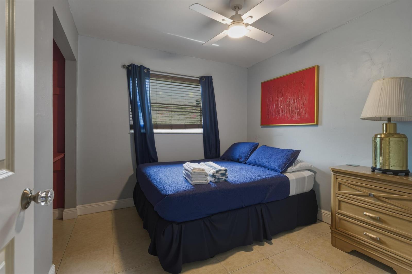 A bedroom features a bed with blue bedding, a ceiling fan, and a wooden dresser — 224 NW 9th Street, Pompano Beach FL 33060, POMPANO BEACH, FL