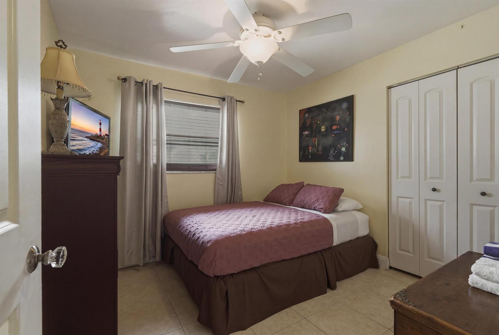 A bedroom features a bed with a mauve quilt, tile flooring, and a ceiling fan — 224 NW 9th Street, Pompano Beach FL 33060, POMPANO BEACH, FL