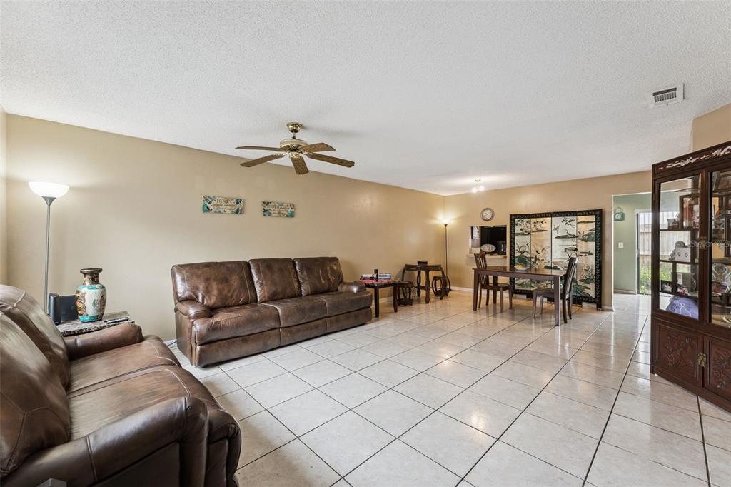 A living room with light tile floors, brown leather sofas, and a dining area — 6297 RIVER RUN PLACE UNIT 197, ORLANDO, FL