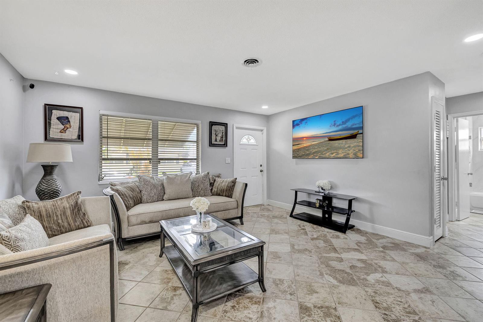 A living room features light gray walls, tile flooring, a sofa, and a wall-mounted television — 4901 NW 27th Way, Tamarac FL 33309, TAMARAC, FL