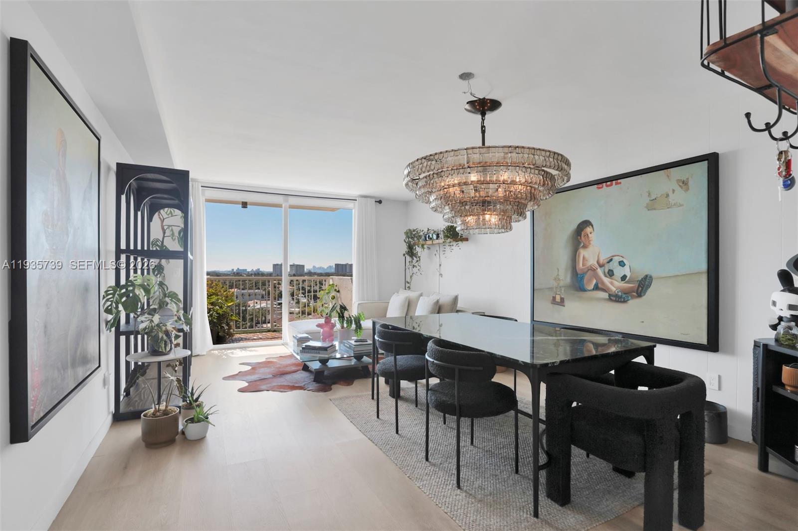 A dining and living area features a large crystal chandelier, modern furniture, and a balcony — 2000 NE 135th St # 908, North Miami FL 33181, NORTH MIAMI, FL