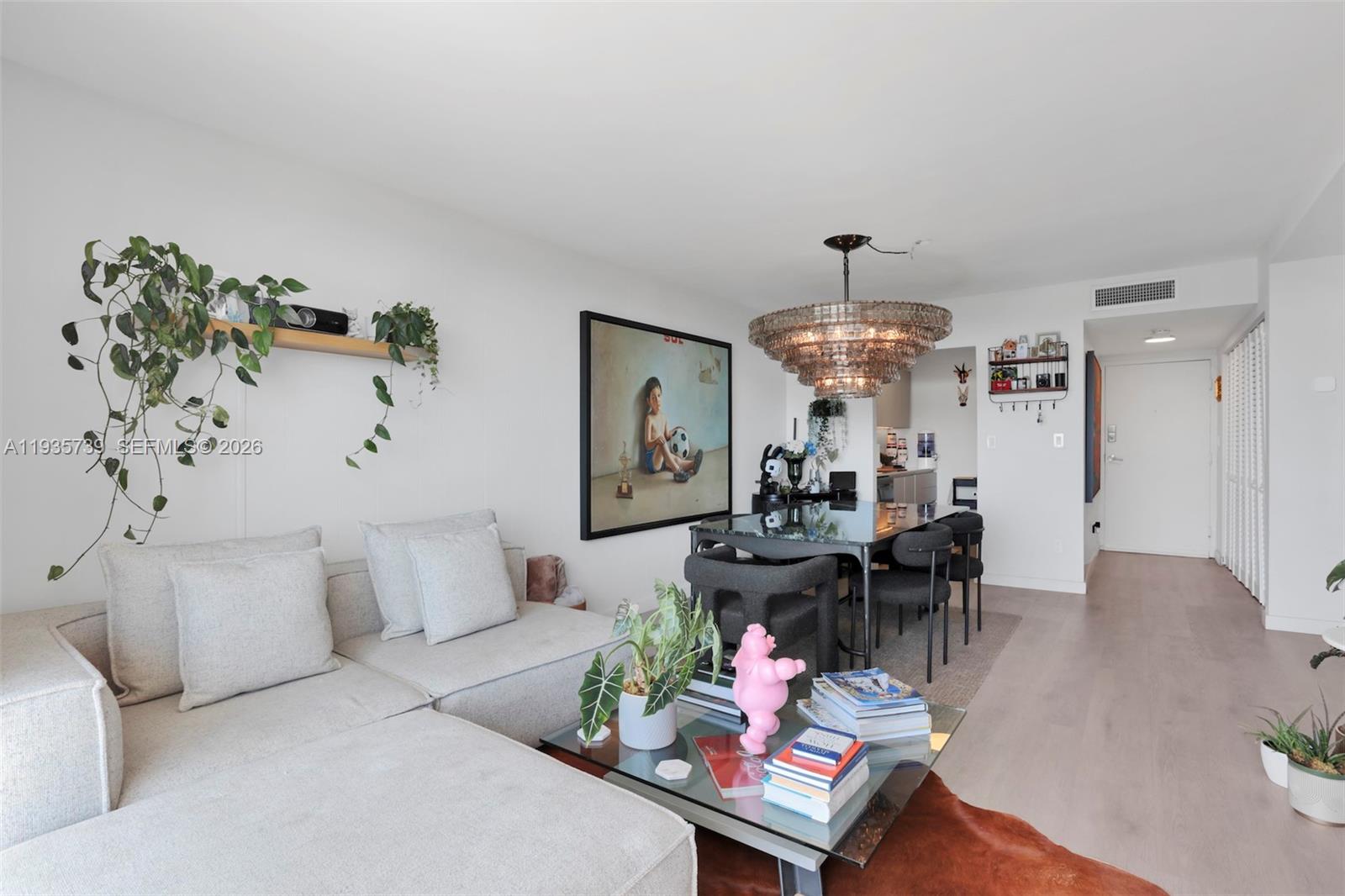 A living and dining area features a light gray sectional sofa, glass coffee table, and chandelier — 2000 NE 135th St # 908, North Miami FL 33181, NORTH MIAMI, FL