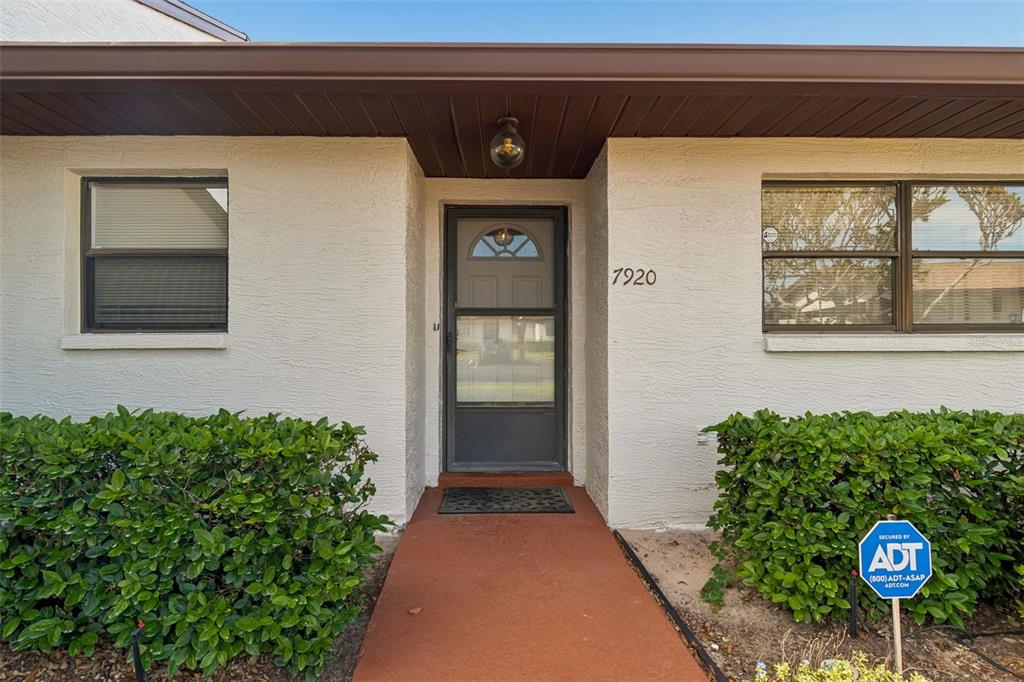 The exterior of a house features a front door, two windows, and a small walkway — 7920 RADCLIFFE CIRCLE, PORT RICHEY, FL