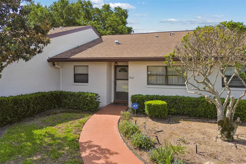 A single-story house with a tan stucco exterior, brown roof, and a curved walkway — 7920 RADCLIFFE CIRCLE, PORT RICHEY, FL