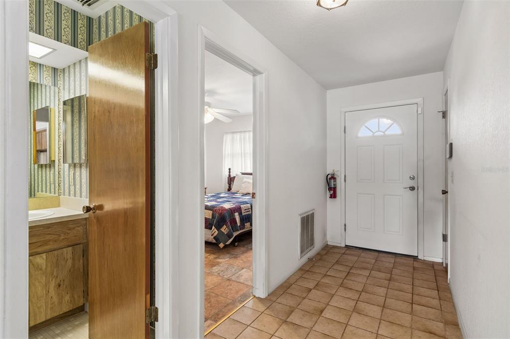 A tiled entryway features a white front door, a fire extinguisher, and an adjacent bathroom — 7920 RADCLIFFE CIRCLE, PORT RICHEY, FL
