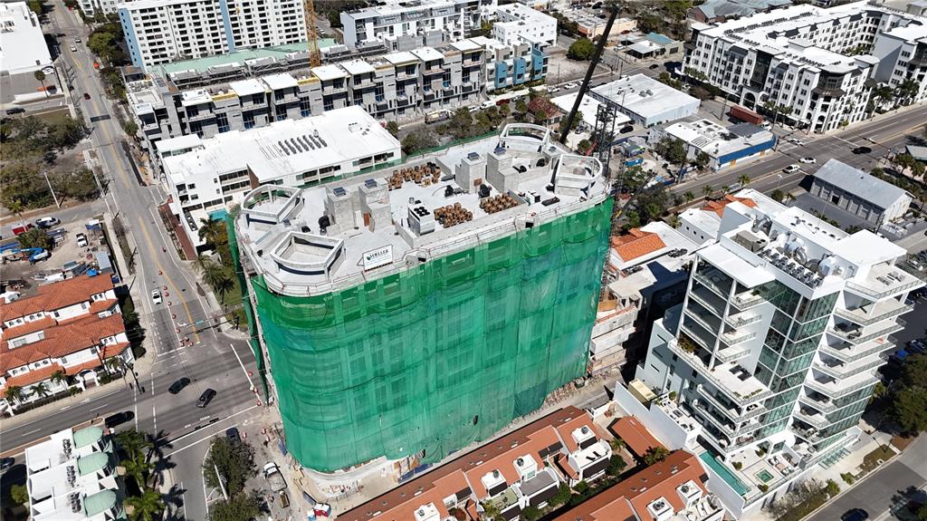An aerial view shows a multi-story building under construction wrapped in green safety netting — 290 COCOANUT AVENUE UNIT 703, SARASOTA, FL